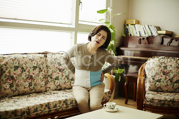 고통 50대 여자 중년 중년여자한명만 한국인 한명 JPG 앞모습 포토 갱년기 디스크(질병) 상반신 소파 실내 앉기 중년라이프 찡그림 컵 허리 허리디스크 허리통증