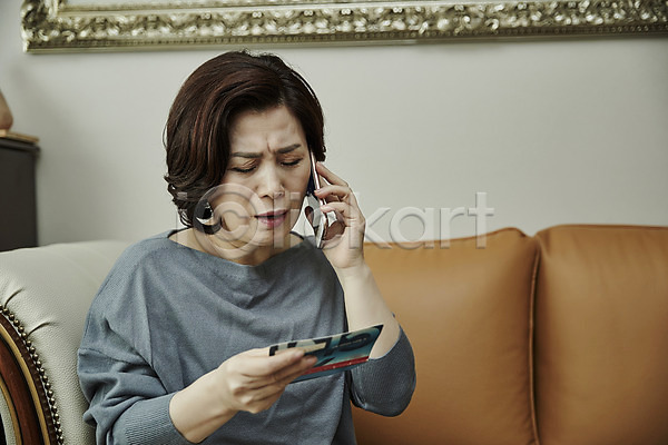 범죄 50대 여자 중년 중년여자한명만 한국인 한명 JPG 앞모습 포토 거실 들기 보이스피싱 상반신 소파 스마트폰 실내 앉기 응시 중년라이프 찡그림 통장 통화