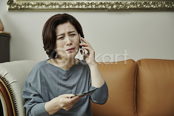 범죄 50대 여자 중년 중년여자한명만 한국인 한명 JPG 앞모습 포토 거실 들기 보이스피싱 상반신 소파 스마트폰 실내 앉기 중년라이프 찡그림 통장 통화