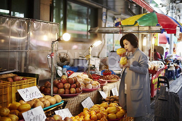 50대 여자 중년 중년여자한명만 한국인 한명 JPG 아웃포커스 옆모습 포토 과일 냄새 들기 상반신 서기 시장 야외 응시 장보기 주간 중년라이프 참외