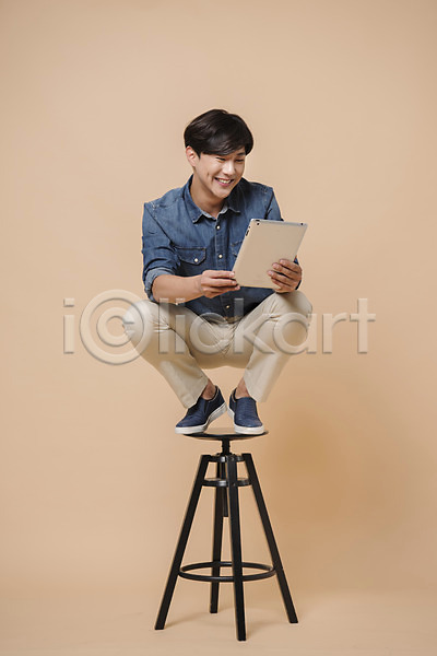 20대 남자 남자한명만 성인 성인남자한명만 한국인 한명 JPG 앞모습 포토 들기 모션 베이지색배경 스튜디오촬영 실내 앉기 웃음 의자 전신 컬러 태블릿 표정