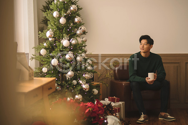 휴식 20대 남자 성인 성인남자한명만 한국인 한명 JPG 아웃포커스 앞모습 포토 거실 들기 미소(표정) 선물 소파 실내 앉기 응시 전신 커피잔 크리스마스 크리스마스트리
