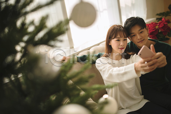 다정 20대 30대 남자 두명 성인 성인만 여자 한국인 JPG 아웃포커스 앞모습 포토 거실 들기 미소(표정) 상반신 셀프카메라 스마트폰 실내 앉기 커플 크리스마스 크리스마스트리