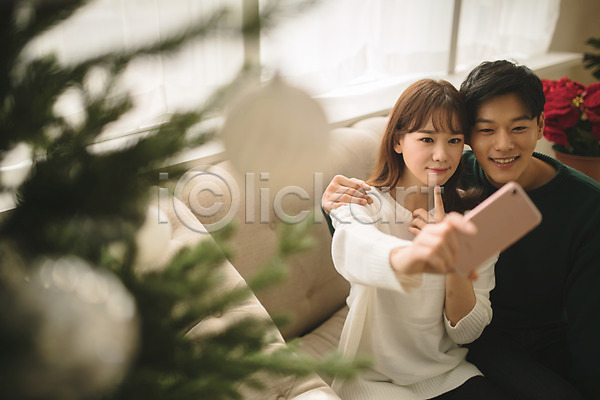 다정 20대 30대 남자 두명 성인 성인만 여자 한국인 JPG 아웃포커스 앞모습 포토 거실 들기 미소(표정) 상반신 셀프카메라 스마트폰 실내 앉기 커플 크리스마스 크리스마스트리