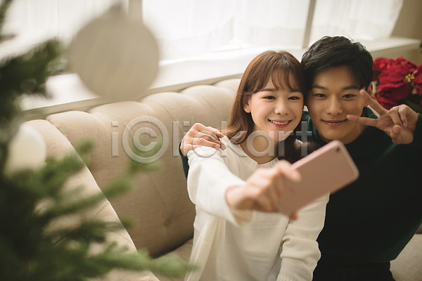 다정 20대 30대 남자 두명 성인 성인만 여자 한국인 JPG 아웃포커스 앞모습 포토 거실 들기 미소(표정) 브이 상반신 셀프카메라 스마트폰 실내 앉기 커플 크리스마스 크리스마스트리