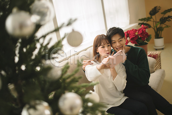 다정 20대 30대 남자 두명 성인 성인만 여자 한국인 JPG 아웃포커스 앞모습 포토 거실 들기 미소(표정) 브이 상반신 셀프카메라 스마트폰 실내 앉기 커플 크리스마스 크리스마스트리