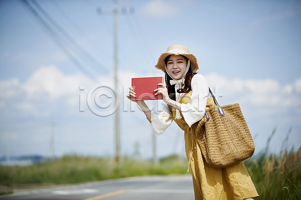 20대 사람 성인여자한명만 여자 한국인 한명 JPG 앞모습 포토 갈대습지 구름(자연) 도로 들기 맑음 미소(표정) 상반신 야외 여름(계절) 우음도 전봇대(시설물) 주간 책 챙모자 하늘 히치하이킹 힐링
