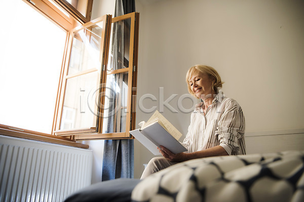 70대 노년 노인여자한명만 사람 서양인 여자 한명 JPG 로우앵글 옆모습 포토 독서 들기 미소(표정) 상반신 실내 실버라이프 앉기 주간 창문 책 침대 침실 커튼