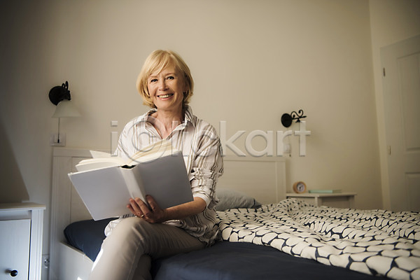 70대 노년 노인여자한명만 사람 서양인 여자 한명 JPG 앞모습 포토 독서 들기 미소(표정) 상반신 실내 실버라이프 앉기 응시 조명 주간 책 침대 침실 탁자