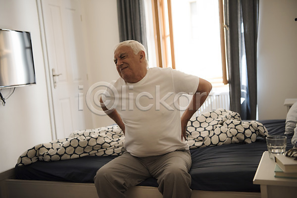 고통 70대 남자 노년 노인남자한명만 사람 서양인 한명 JPG 앞모습 포토 물컵 상반신 실버라이프 앉기 찡그림 창문 책더미 침대 침실 커튼 탁자 허리통증
