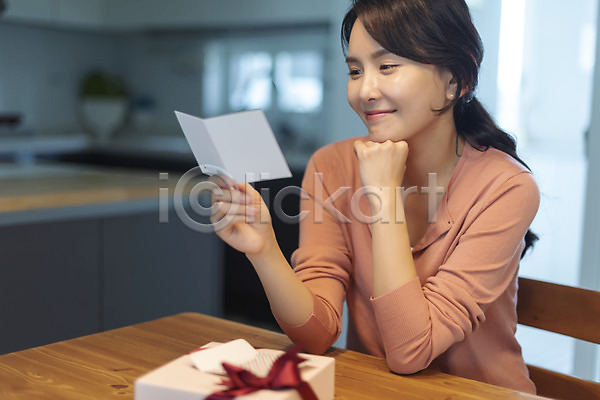 기쁨 30대 사람 성인 성인여자한명만 여자 한국인 한명 JPG 앞모습 포토 미소(표정) 상반신 선물 실내 앉기 엄마 응시 읽기 주방 주부 턱괴기 편지
