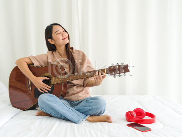 휴식 동양인 성인 성인여자한명만 여자 한명 JPG 앞모습 포토 해외이미지 기타 기타리스트 스마트폰 실내 앉기 연주 전신 취미 침대 헤드폰