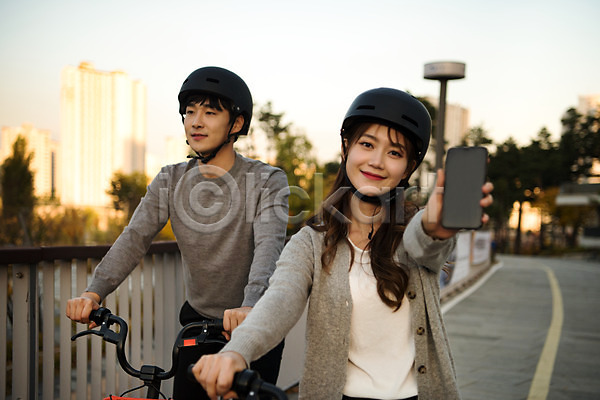 사랑 설레임 즐거움 행복 20대 남자 두명 사람 성인 성인만 여자 한국인 JPG 앞모습 포토 공원 공유자전거 광교호수공원 데이트 들기 미소(표정) 상반신 손내밀기 수원 스마트폰 안전 야외 운동 응시 자전거 주간 커플 헬멧