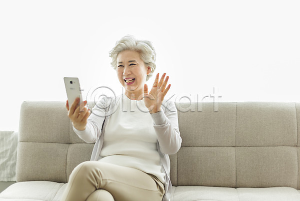 60대 노년 노인여자한명만 사람 여자 한국인 한명 JPG 앞모습 포토 다리꼬기 들기 미소(표정) 상반신 소파 손인사 스마트폰 스튜디오촬영 실내 실버라이프 앉기 영상통화 응시 인사 일상 할머니