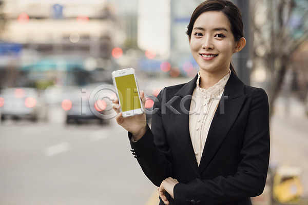 스마트 20대 사람 성인 성인여자한명만 여자 한국인 한명 JPG 아웃포커스 앞모습 포토 들기 미소(표정) 버스정류장 비즈니스 비즈니스우먼 상반신 서기 스마트폰 야외 어플리케이션 예약 정장 주간 카쉐어링 카풀 확인