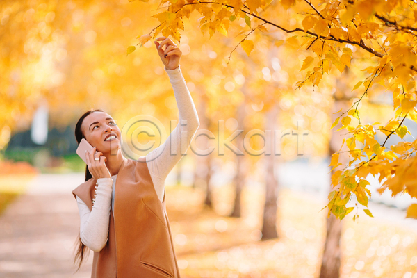 산책 성인 성인여자한명만 여자 한명 JPG 아웃포커스 앞모습 포토 해외이미지 가을(계절) 공원 노란색 단풍 단풍나무 들기 미소(표정) 상반신 손뻗기 스마트폰 올려보기 잡기 통화