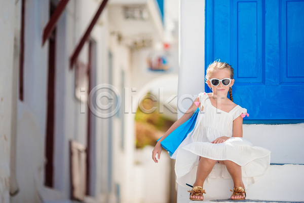 휴식 소녀(어린이) 소녀한명만 어린이 여자 한명 JPG 앞모습 포토 해외이미지 골목길 문 미코노스섬 바캉스 선글라스 쇼핑백 앉기 야외 여름(계절) 여름휴가 원피스 전신 주간 파란색 흰색