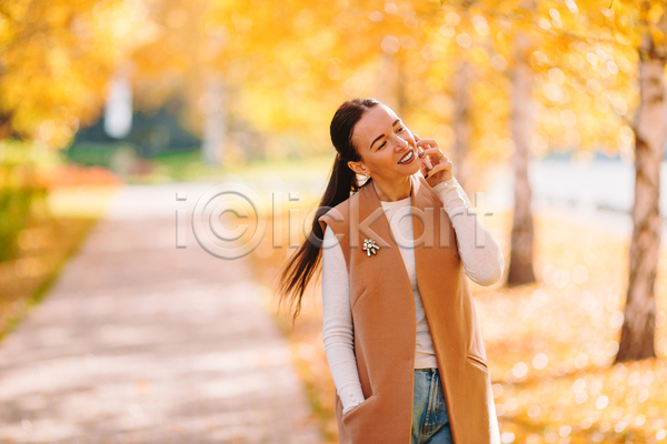 성인 성인여자한명만 여자 한명 JPG 아웃포커스 앞모습 포토 해외이미지 가을(계절) 공원 들기 미소(표정) 산책로 상반신 스마트폰 주머니손 통화