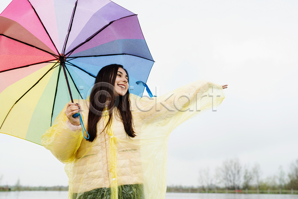 성인 성인여자한명만 여자 한명 JPG 앞모습 포토 해외이미지 들기 비(날씨) 상반신 손들기 야외 우비 우산 웃음 주간 하늘