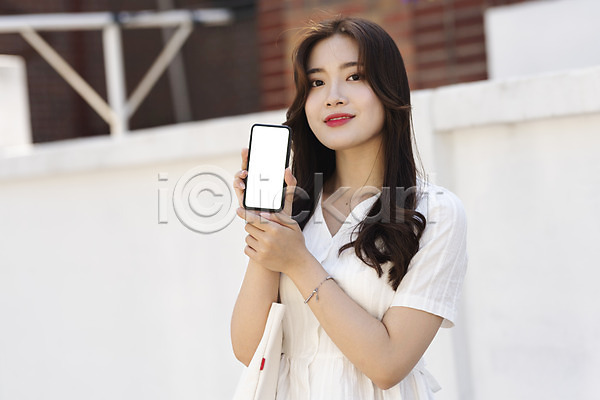 스마트 즐거움 20대 성인 성인여자한명만 여자 한국인 한명 JPG 앞모습 포토 거리 들기 미소(표정) 보여주기 상반신 서기 스마트폰 싱글라이프 야외 에코백 여름(계절) 우먼라이프 인싸 주간 캐주얼