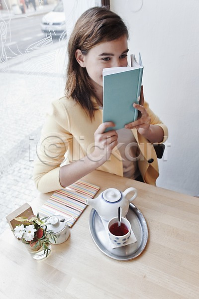 즐거움 편안함 휴식 20대 서양인 성인 성인여자한명만 여자 외국인 한명 JPG 앞모습 포토 하이앵글 독서 들기 미소(표정) 상반신 실내 앉기 우먼라이프 차(자동차) 찻주전자 책 카페 컬러풀 탁자