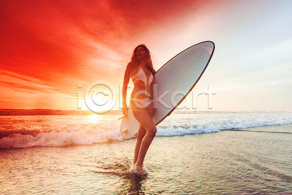 성인 성인여자한명만 여자 한명 JPG 앞모습 포토 해외이미지 걷기 노을 들기 바다 서기 서핑 서핑보드 수영복 수평선 야외 전신 주간 태양 파도 하늘