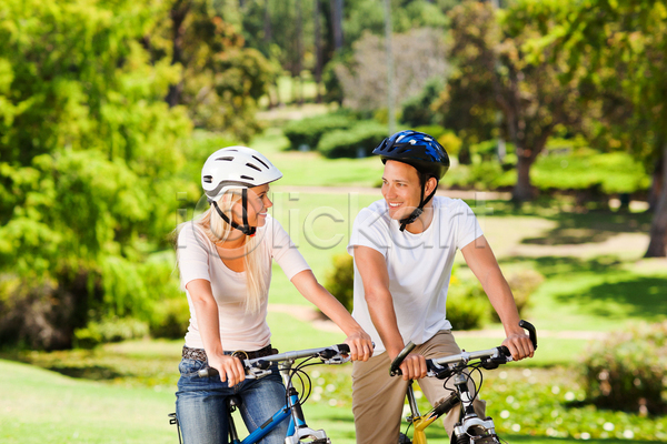 남자 두명 백인 성인 성인만 여자 JPG 앞모습 포토 해외이미지 건강관리 공원 마주보기 상반신 야외 웃음 응시 자전거 잡기 주간 커플 커플라이프 헬멧
