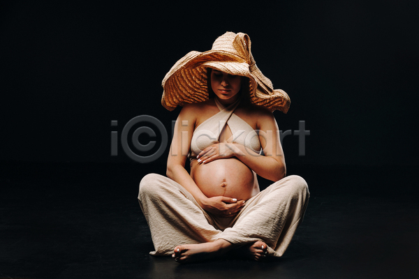 성인 성인여자한명만 여자 한명 JPG 앞모습 포토 해외이미지 가부좌 감싸기 검은배경 그림자 밀짚모자 실내 앉기 임산부 임신 전신 포즈