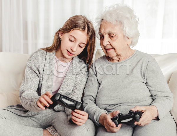 노년 두명 소녀(어린이) 어린이 여자 여자만 JPG 앞모습 포토 해외이미지 가르침 가족 게임기 게임콘트롤러 들기 미소(표정) 상반신 소파 손녀 실내 앉기 응시 조부모 할머니