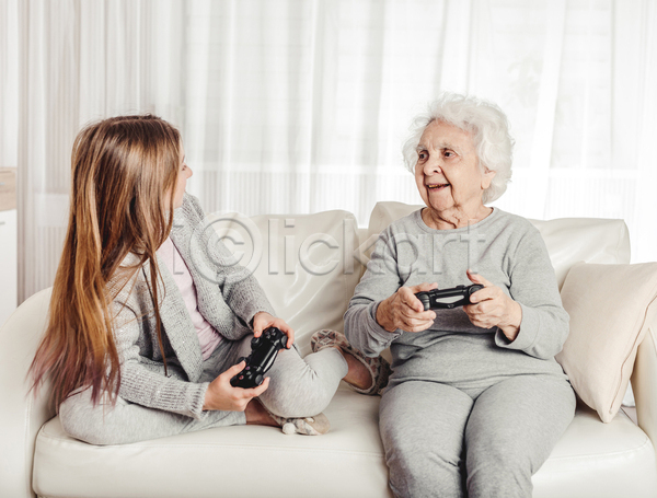 노년 두명 소녀(어린이) 어린이 여자 여자만 JPG 앞모습 옆모습 포토 해외이미지 가족 게임기 게임콘트롤러 들기 미소(표정) 상반신 소파 손녀 실내 앉기 응시 전신 조부모 할머니