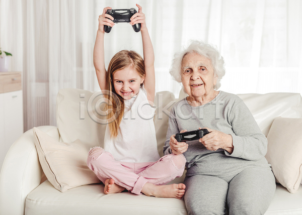 노년 두명 소녀(어린이) 어린이 여자 여자만 JPG 앞모습 포토 해외이미지 가족 게임기 게임콘트롤러 들기 미소(표정) 상반신 소파 손녀 손들기 실내 앉기 응시 전신 조부모 쿠션 할머니