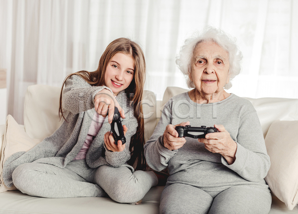 노년 두명 소녀(어린이) 어린이 여자 여자만 JPG 포토 해외이미지 가족 게임 게임기 게임콘트롤러 들기 미소(표정) 상반신 소파 손녀 실내 앉기 응시 전신 조부모 쿠션 할머니