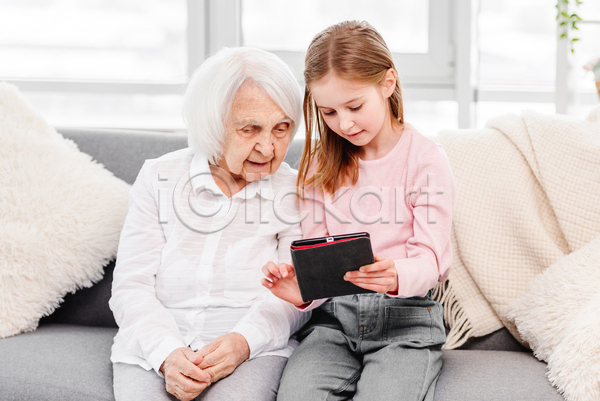 노년 두명 소녀(어린이) 어린이 여자 여자만 JPG 앞모습 포토 해외이미지 가르침 가족 들기 미소(표정) 소파 손녀 실내 앉기 조부모 태블릿 할머니