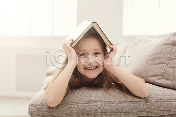즐거움 백인 소녀(어린이) 소녀한명만 어린이 여자 한명 JPG 앞모습 포토 해외이미지 독서 미소(표정) 상반신 소파 실내 엎드리기 책