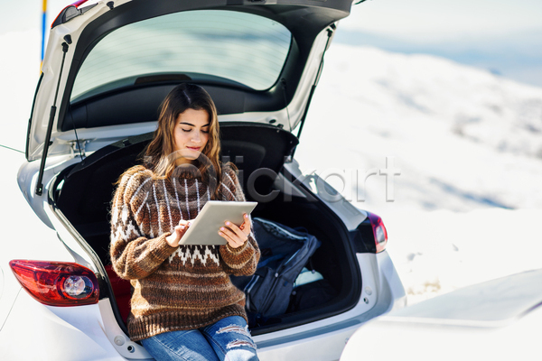 휴식 성인 성인여자한명만 여자 한명 JPG 아웃포커스 앞모습 포토 해외이미지 걸터앉기 겨울 들기 상반신 스웨터 야외 응시 자동차 자동차트렁크 주간 태블릿