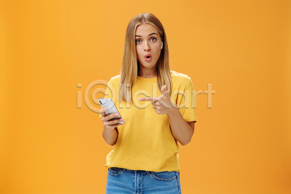 성인 성인여자한명만 여자 한명 JPG 앞모습 포토 해외이미지 가리킴 노란색 노래감상 들기 무선이어폰 상반신 스마트폰 실내
