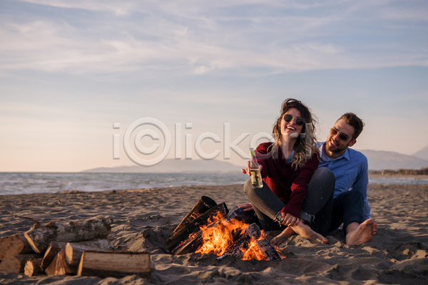 남자 두명 성인 성인만 여자 JPG 앞모습 포토 해외이미지 들기 모닥불 앉기 야간 야외 웃음 음료수병 전신 캠핑 커플 하늘 해변