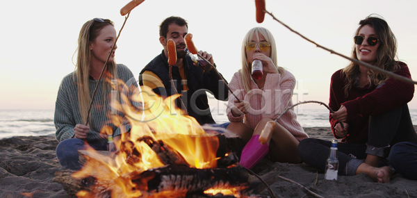 남자 성인 성인만 여러명 여자 JPG 앞모습 포토 해외이미지 굽기 나뭇가지 들기 마시기 맥주 모닥불 소시지 앉기 야외 전신 주간 친구 캠핑 해변