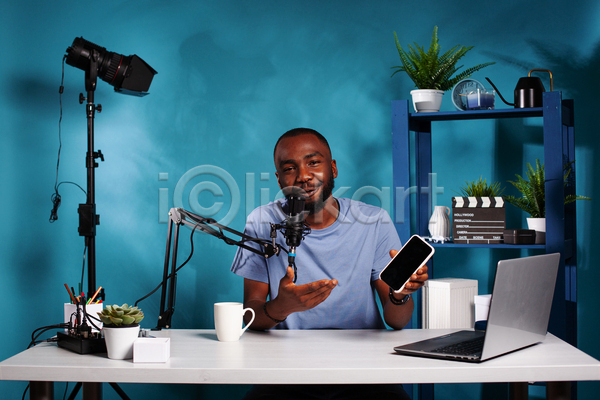 남자 성인 성인남자한명만 한명 JPG 앞모습 포토 해외이미지 노트북 들기 마이크 말하기 방송 상반신 선반 스마트폰 유튜버 책상 촬영 촬영실 컵 파란색 화초
