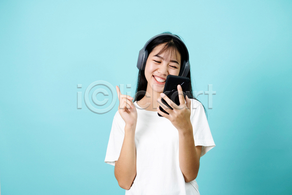 즐거움 성인 성인여자한명만 여자 한명 JPG 앞모습 포토 해외이미지 가리킴 들기 상반신 스마트폰 실내 웃음 음악감상 파란배경 헤드셋