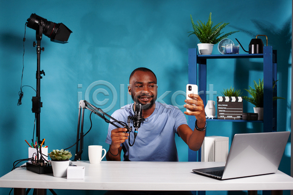 남자 성인 성인남자한명만 한명 JPG 앞모습 포토 해외이미지 노트북 마이크 방송 상반신 선반 셀프카메라 스마트폰 유튜버 책상 촬영 촬영실 컵 파란색 화초