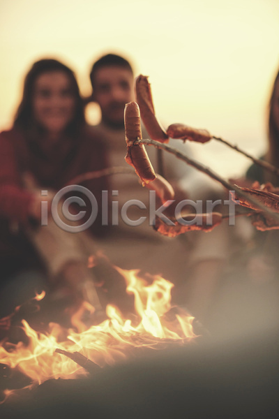 남자 두명 성인 성인만 여자 JPG 소프트포커스 아웃포커스 앞모습 포토 해외이미지 굽기 나뭇가지 들기 모닥불 상반신 소시지 소시지구이 야외 주간 캠핑 해변