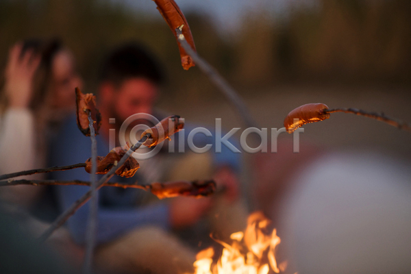 남자 두명 성인 성인만 여자 JPG 소프트포커스 아웃포커스 옆모습 포토 해외이미지 굽기 나뭇가지 모닥불 상반신 소시지 소시지구이 야간 야외 캠핑