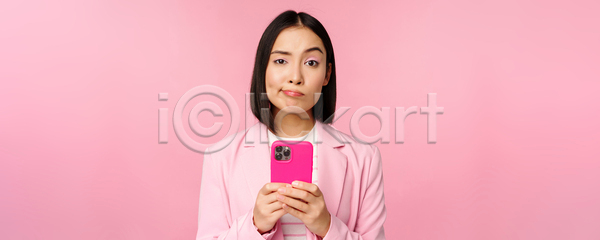 동양인 성인 성인여자한명만 여자 한명 JPG 포토 해외이미지 들기 분홍색배경 비즈니스 비즈니스우먼 상반신 서기 스마트폰 찡그림