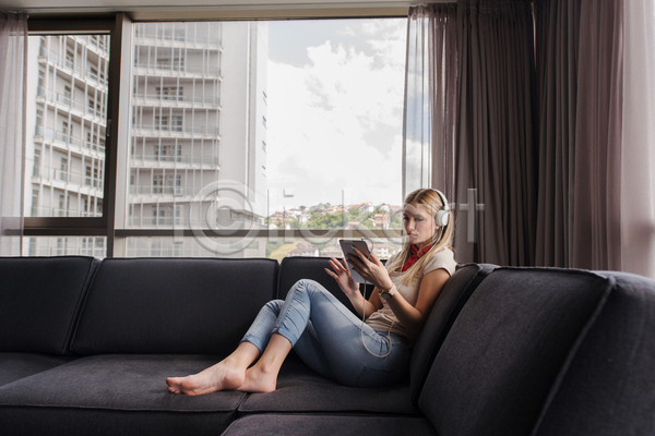 여유 휴식 성인 성인여자한명만 여자 한명 JPG 옆모습 포토 해외이미지 들기 소파 실내 앉기 앳홈라이프 음악감상 전신 집콕 창문 태블릿 헤드셋