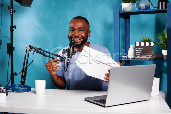 남자 성인 성인남자한명만 한명 JPG 앞모습 포토 해외이미지 노트북 들기 마이크 방송 상반신 상자 선반 유튜버 책상 촬영 촬영실 컵 파란색 화초