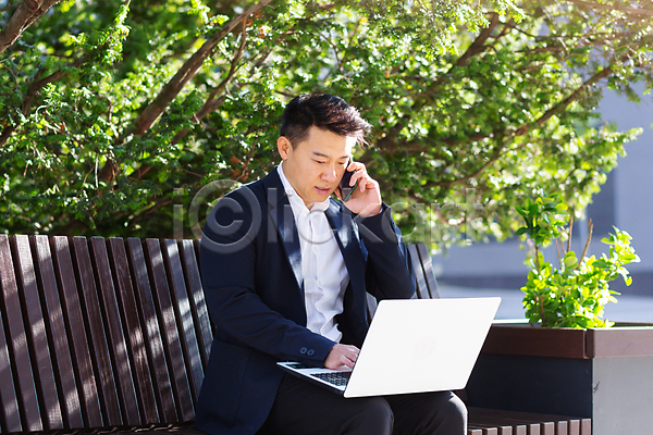 출장 남자 동양인 성인 성인남자한명만 한명 JPG 포토 해외이미지 공원 나무 노트북 들기 벤치 비즈니스맨 스마트폰 앉기 야외 잎 정장 풀(식물) 해외202309 화단