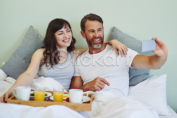 남자 두명 백인 성인 성인만 여자 JPG 앞모습 포토 해외이미지 들기 미소(표정) 부부라이프 상반신 셀프카메라 스마트폰 신혼부부 실내 앉기 음식 침대 커플