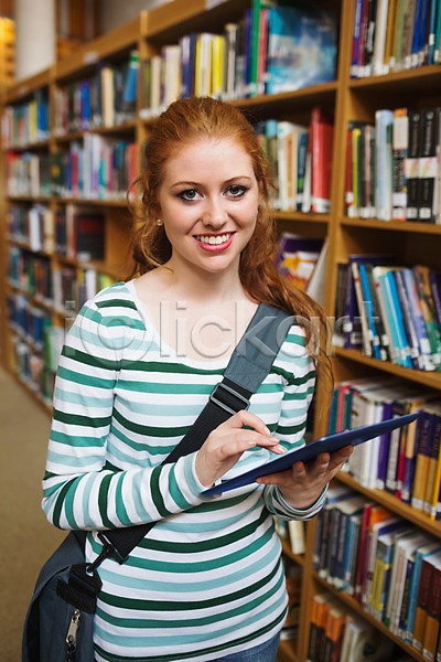 스마트 백인 여자 한명 JPG 포토 해외이미지 교과서 교육 대학교 도서관 미소(표정) 빨간머리 서기 스터디 실내 응시 잡기 정보 책 책장 태블릿 터치 터치스크린 포니테일 학생 해외202004