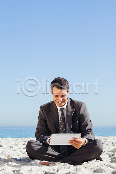 자유 행복 20대 남자 백인 사람 성인 성인남자한명만 한명 JPG 포토 해외이미지 넥타이 맑음 모래 물 미소(표정) 바다 비즈니스맨 앉기 야외 정장 태블릿 터치 파도 하늘 해외202004 햇빛 휴가